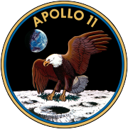 Circular insignia: Eagle with wings outstretched holds olive branch on Moon with earth in background, in blue and gold border.